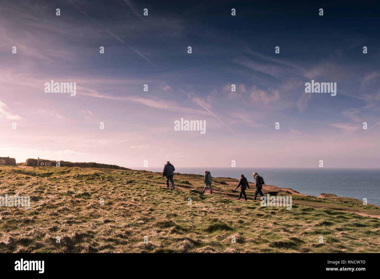 A group of walkers and a dog walking along the South West Coast Path on the North Cornwall coast in late afternoon light. Stock Photo