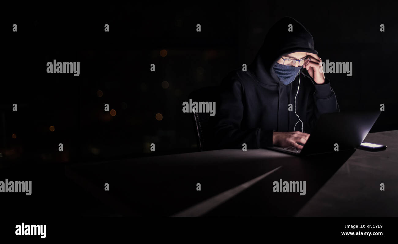 Young talented hacker using laptop computer while working in dark ...