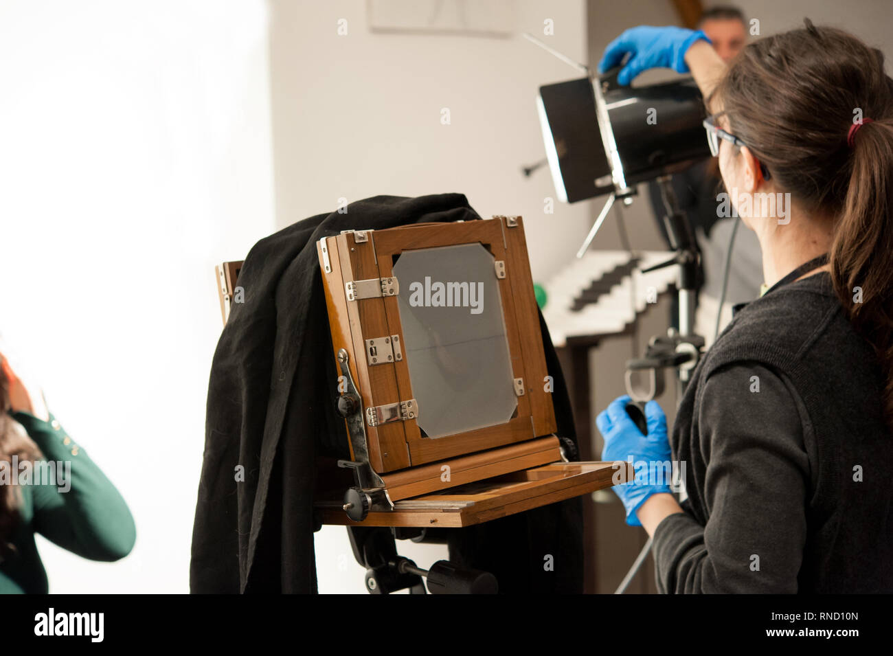 Photographer woman sets the ligths for portrait studio shooting. Large format camera in the foreground. Stock Photo