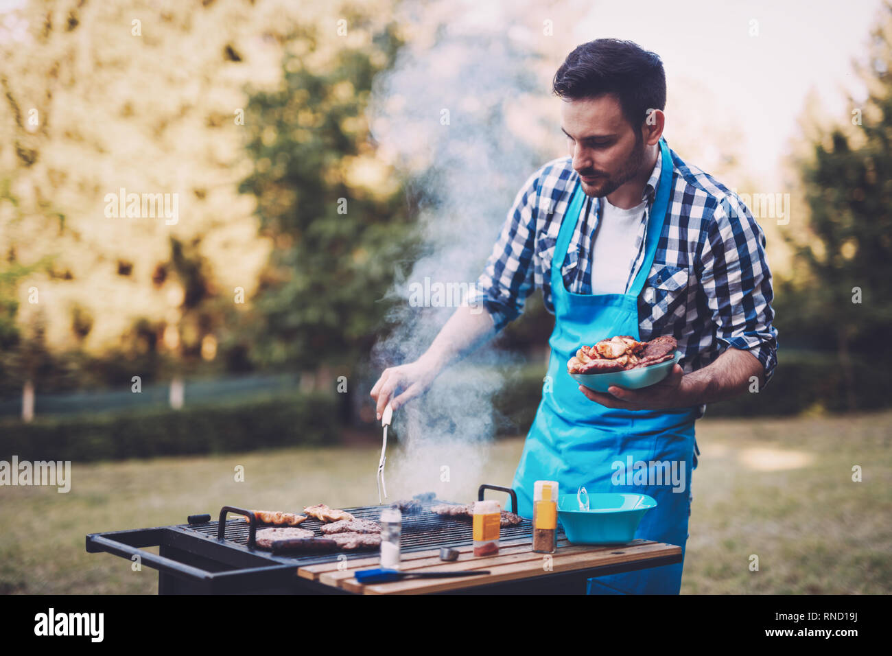 Handsome young male preparing barbecue in forest Stock Photo