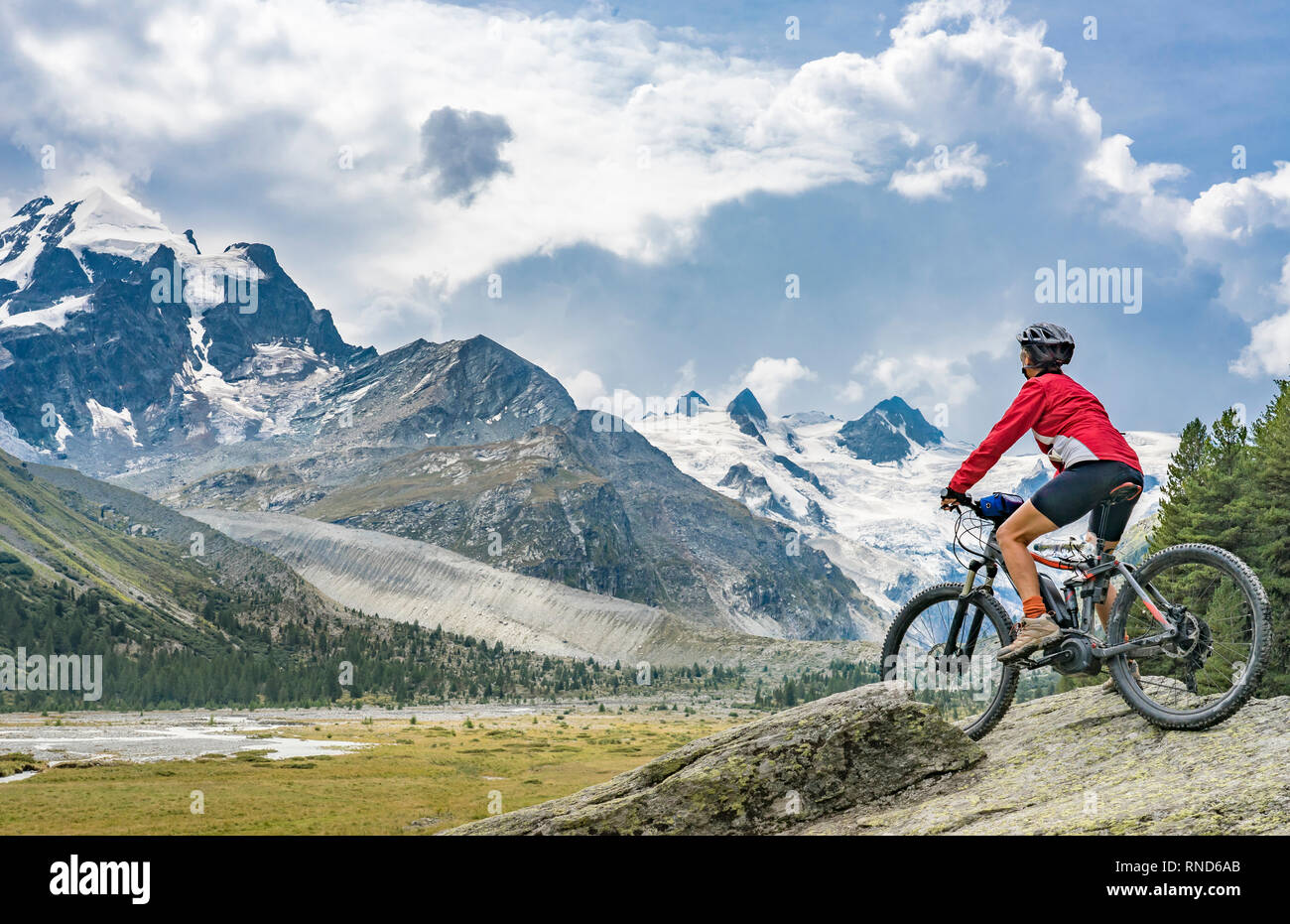 active senior woman, riding her e-mountain bike in the Roseg valley below the glaciers and summits of the Sella Group and Piz Roseg Stock Photo