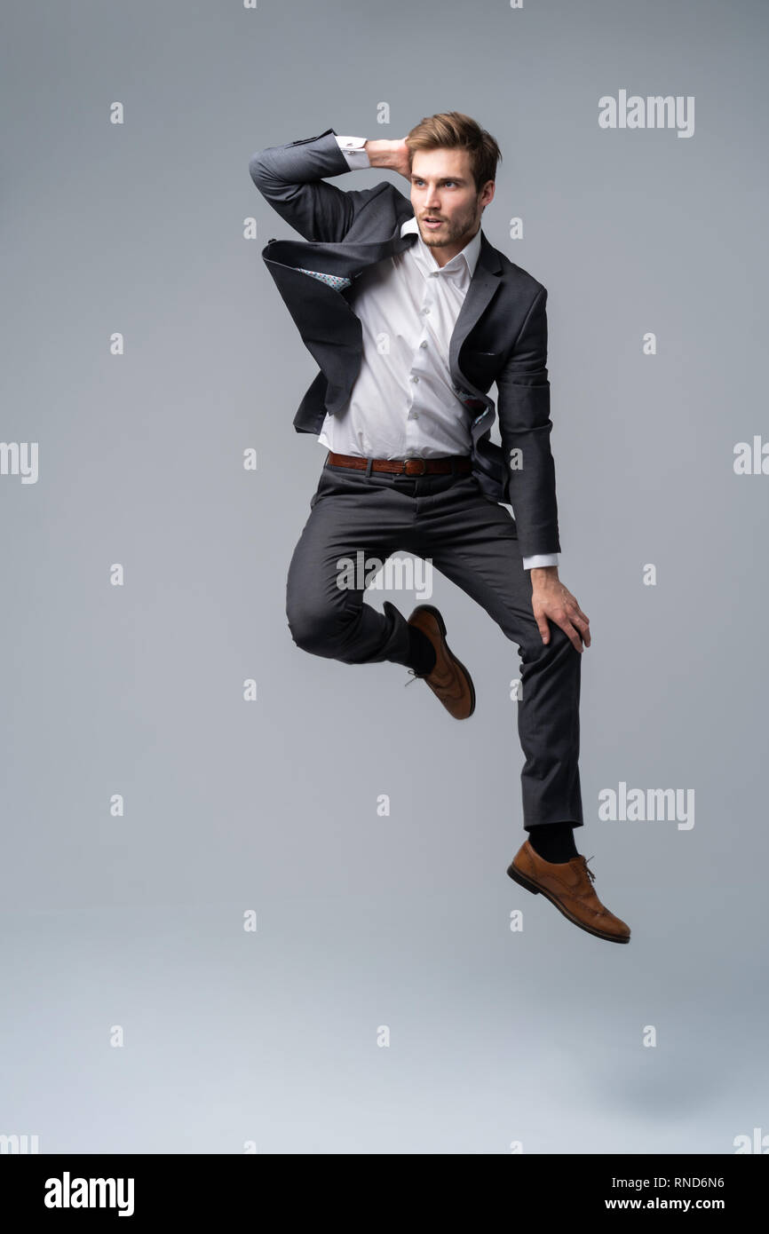 Mid-air style. Handsome young man in full suit jumping against gray background. Stock Photo