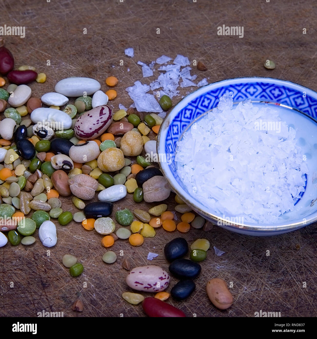 Dried assortment of dry  colourful beans on a wooden surface with a bowl of crystal salt. Stock Image. Stock Photo
