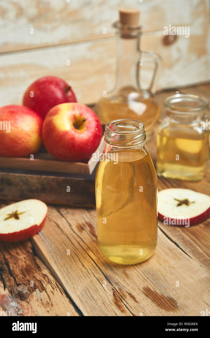 Apple cider vinegar. Glass Bottle of apple organic vinegar on wooden table. Healthy organic drink food. Bottle of fresh cider near autumn red apples.  Stock Photo