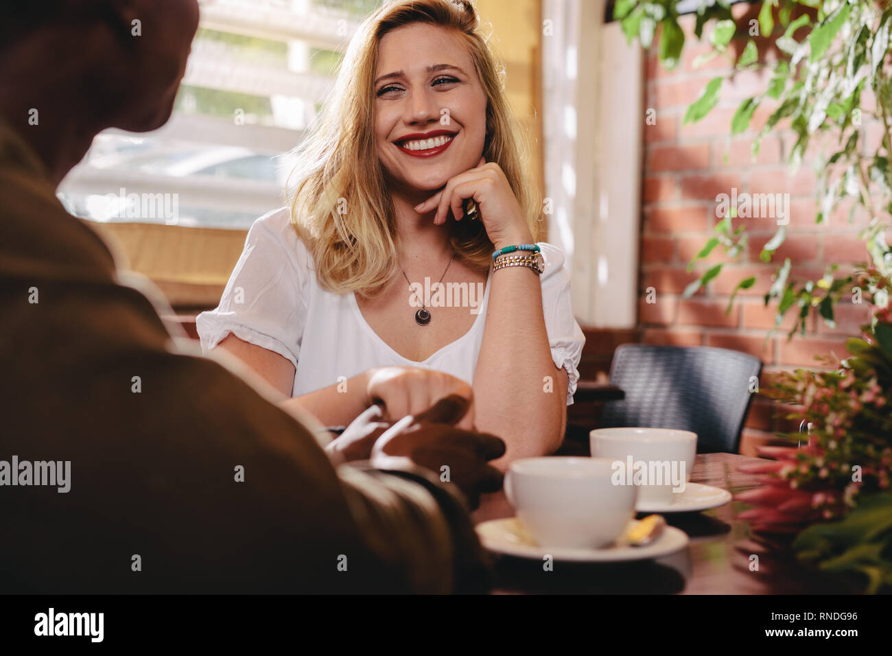 Smiling woman sitting at cafe table holding hand of her boyfriend. Dating couple spending quality time at coffee shop. Stock Photo