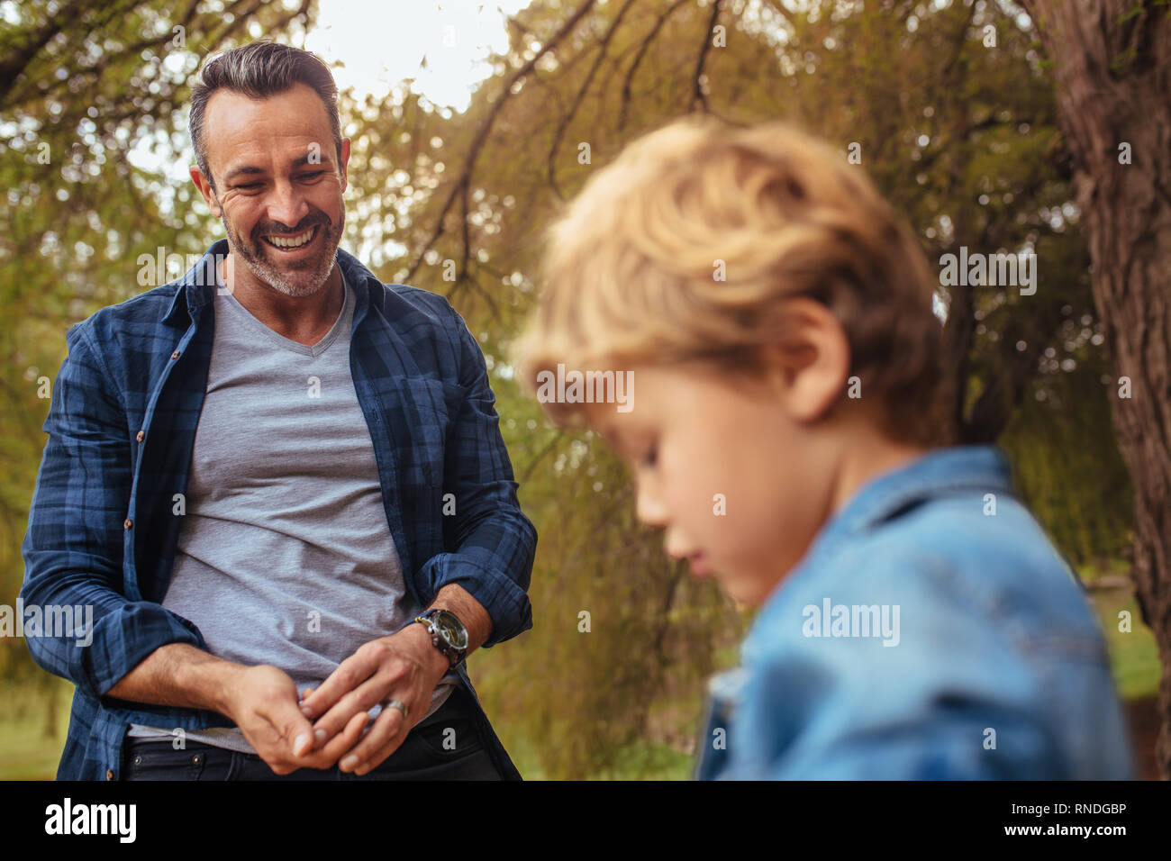 Mature man looking at a little boy in front and smiling at park. Happy father and son at the park. Stock Photo