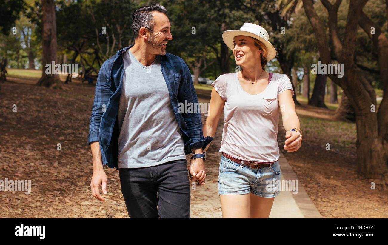 Beautiful couple walking through a park holding hands and looking at ...