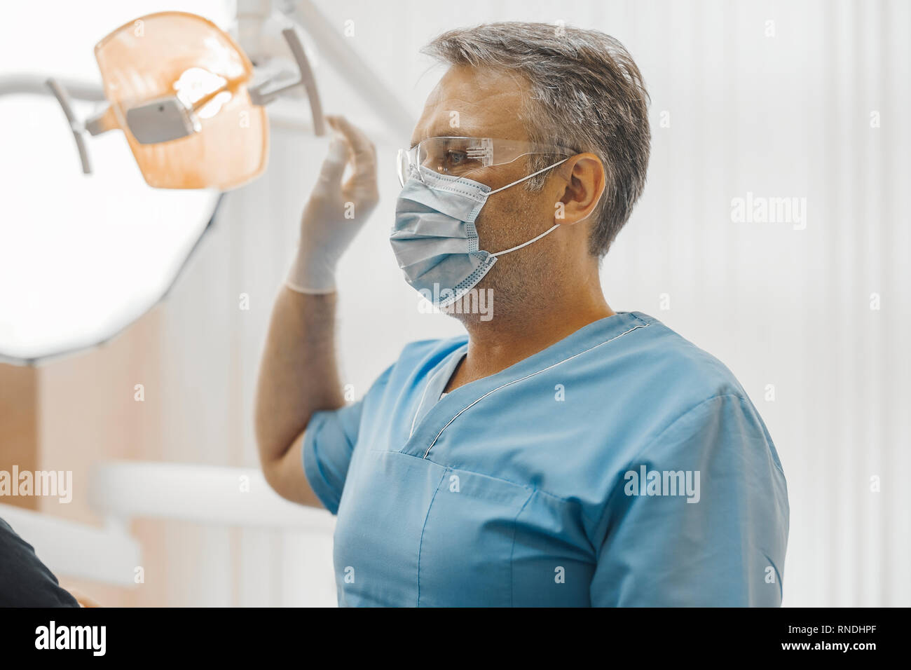 Dentist in blue uniform and transparent glasses sitting next to dental