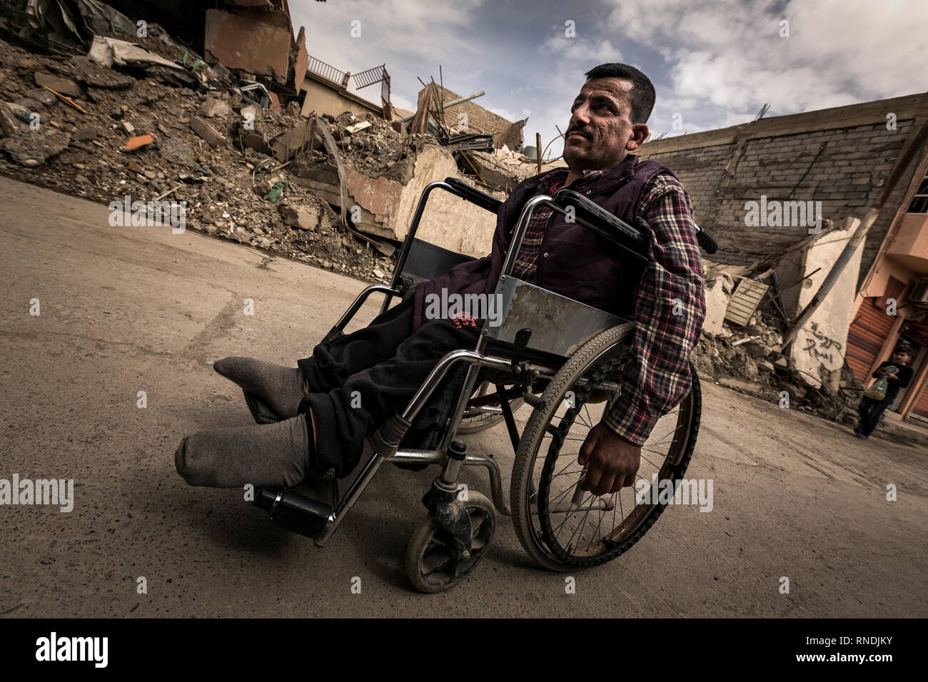 Wheelchair user in the streets of the small Christian town of Bartelle, devastated by the IS, at the gates of Mossul. The Christian population was expelled but returned to their homes in large numbers. Some churches could be rebuilt, so that church services can take place there again. Nevertheless, the Christians are now threatened by the Shiite conquerors of the province of Ninawa and the capital Mossul and are being repressed more and more, so that the Christians do not have good prospects for a further life in Bartella. Stock Photo