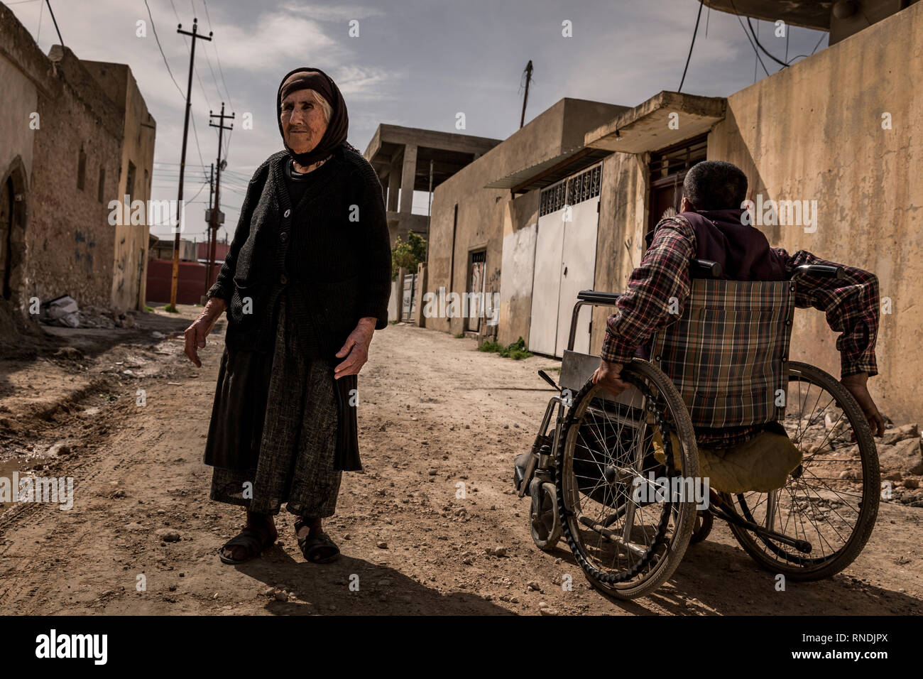 Wheelchair user in the streets of the small Christian town of Bartelle, devastated by the IS, at the gates of Mossul. The Christian population was expelled but returned to their homes in large numbers. Some churches could be rebuilt, so that church services can take place there again. Nevertheless, the Christians are now threatened by the Shiite conquerors of the province of Ninawa and the capital Mossul and are being repressed more and more, so that the Christians do not have good prospects for a further life in Bartella. Stock Photo