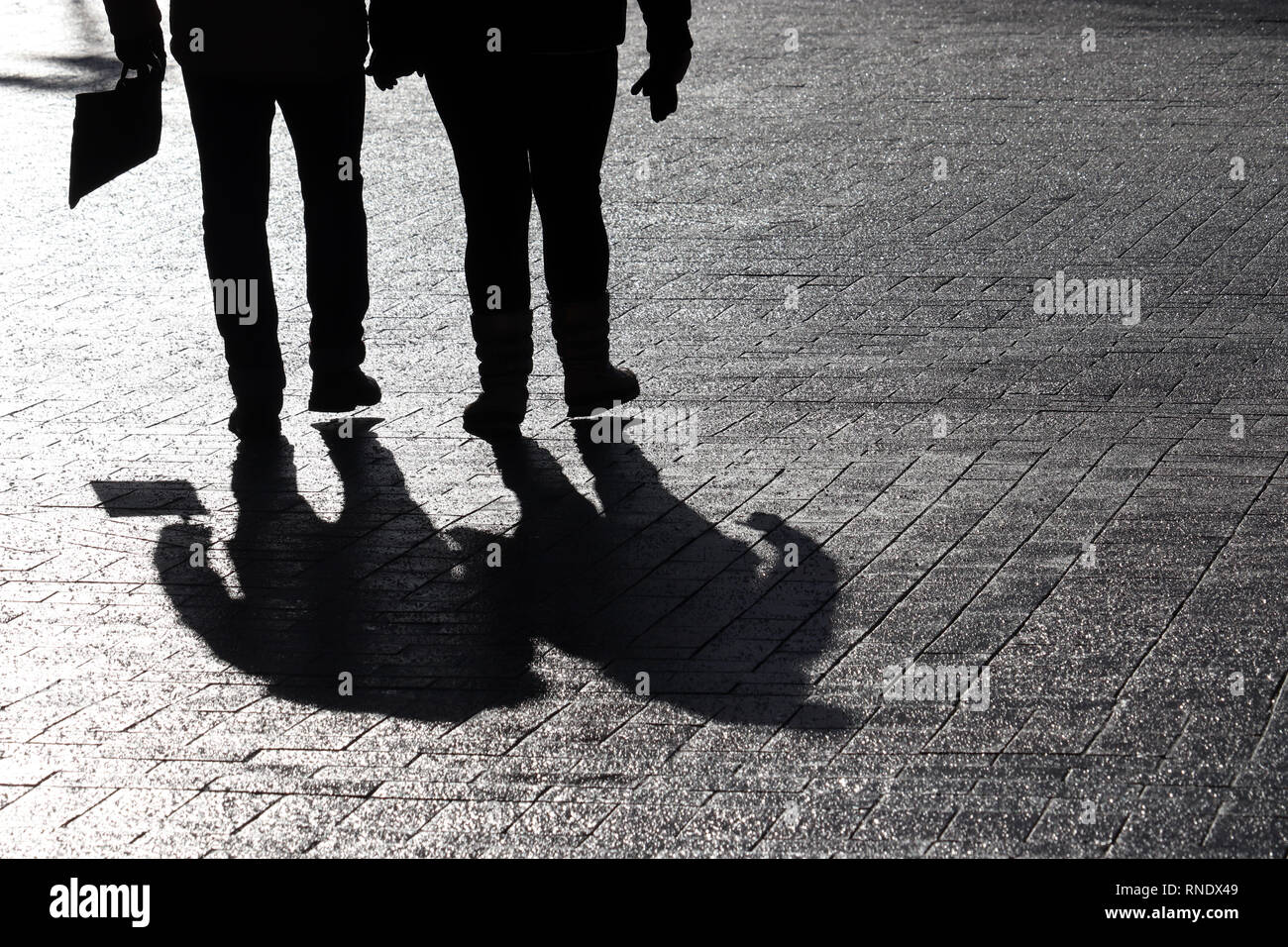 Silhouettes of two people walking down the street. Couple outdoors, people shadows on pavement, concept for for dramatic stories Stock Photo