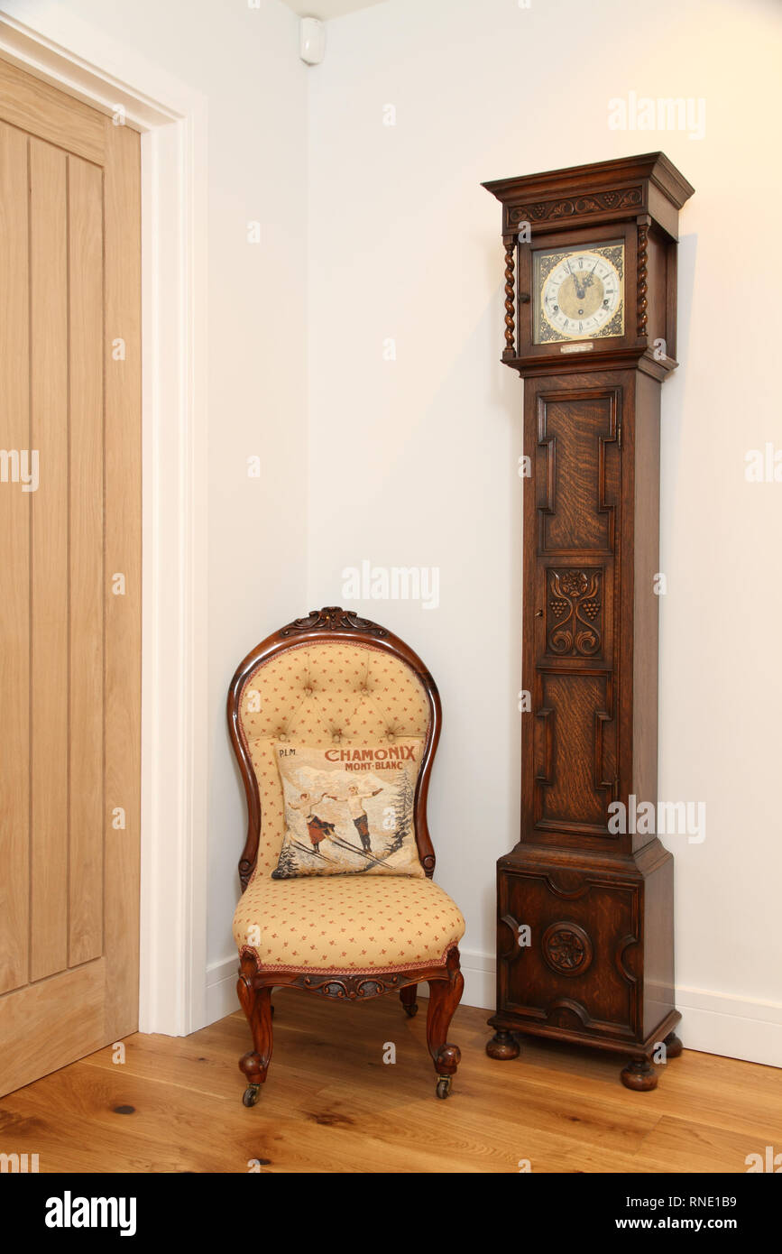 Recovered upright easy chair by a grandmother clock and wooden door Stock Photo