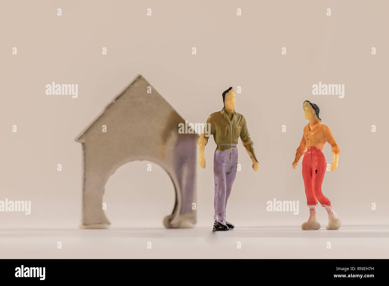 Miniature woman and man figure standing next to house made of coin holder with no coins. Shallow depth of field background. Family budget, mortgage an Stock Photo