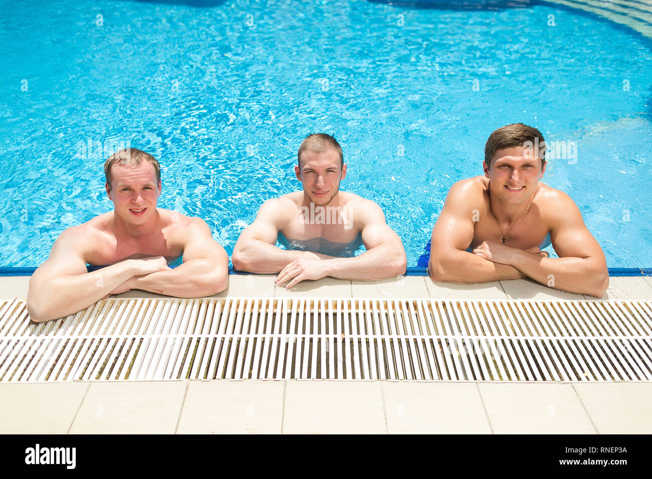 sport, healthy relaxation, party concept. there are three adorable stringly built guys that are holding by the swimming pool nosing and smiling, water Stock Photo