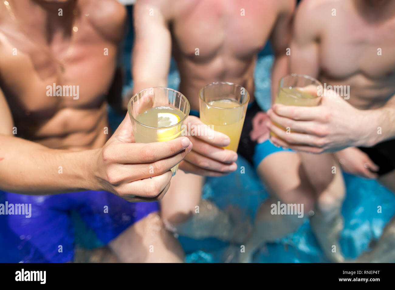 relaxation, party, alcohole concept. close up of glasses that are full with cold fresh cocktails in the hands of three young men with strong bodies wi Stock Photo