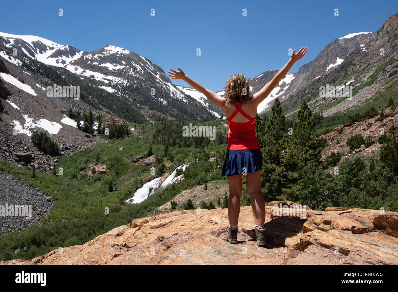 Adult female hiker with back facing the camera, and arms raised in
