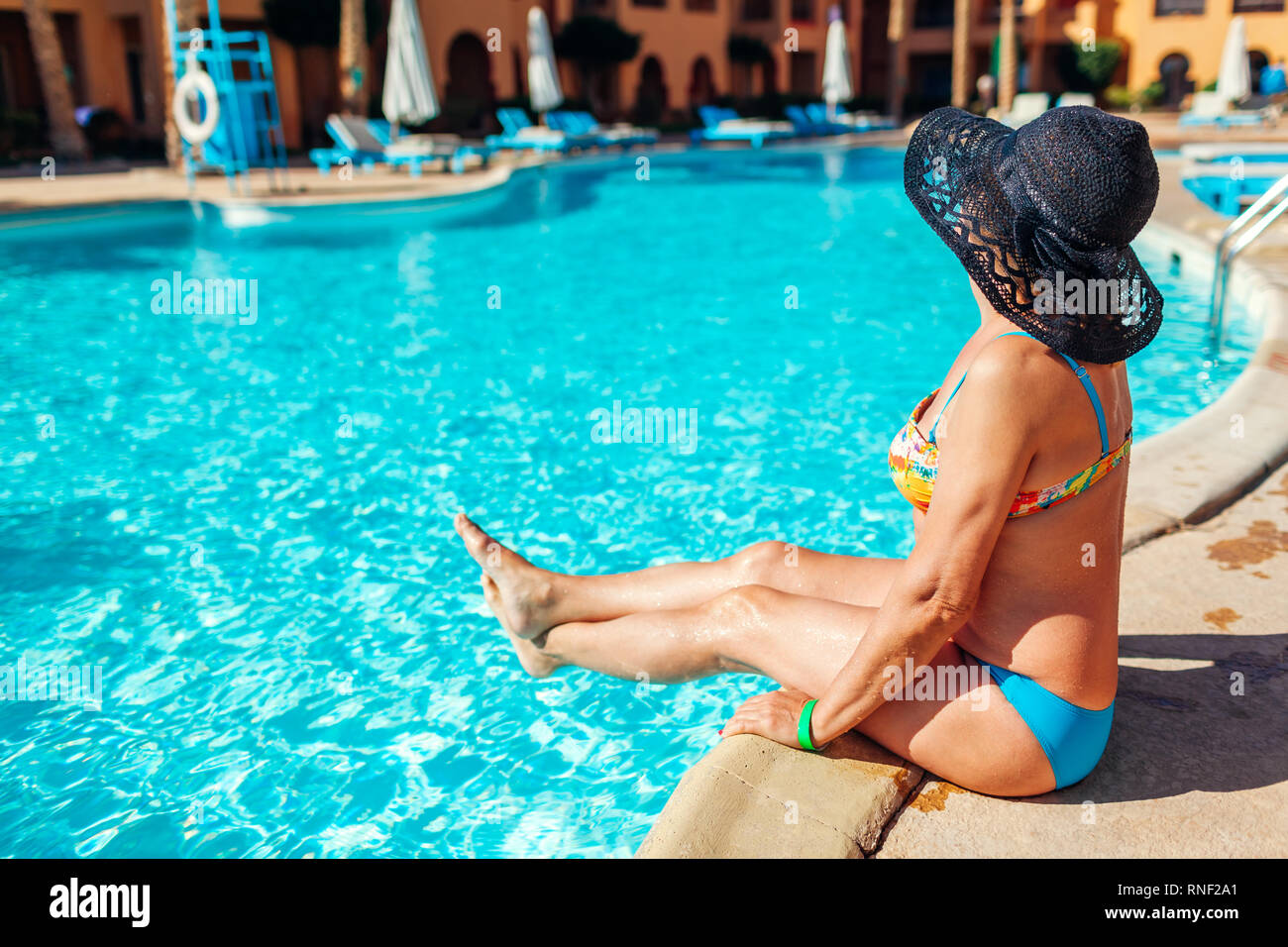 Senior woman in bikini relaxing by hotel swimming pool. People enjoying summer vacation. All inclusive Stock Photo