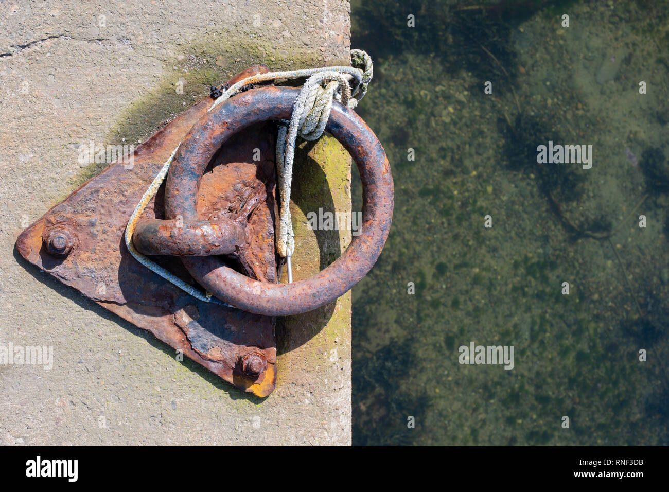 An old and rusty boat mooring ring set into the harbour concrete Stock Photo