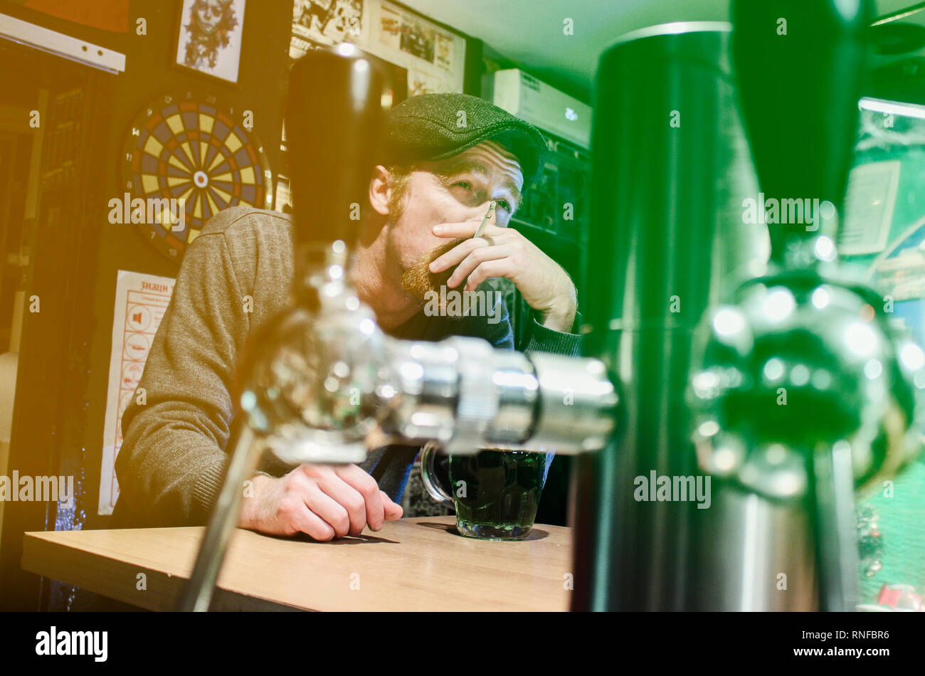 Good guy Irish smokes cigarette and drink beer in pub during St Patrick Day (filter represent Irish flag) Stock Photo