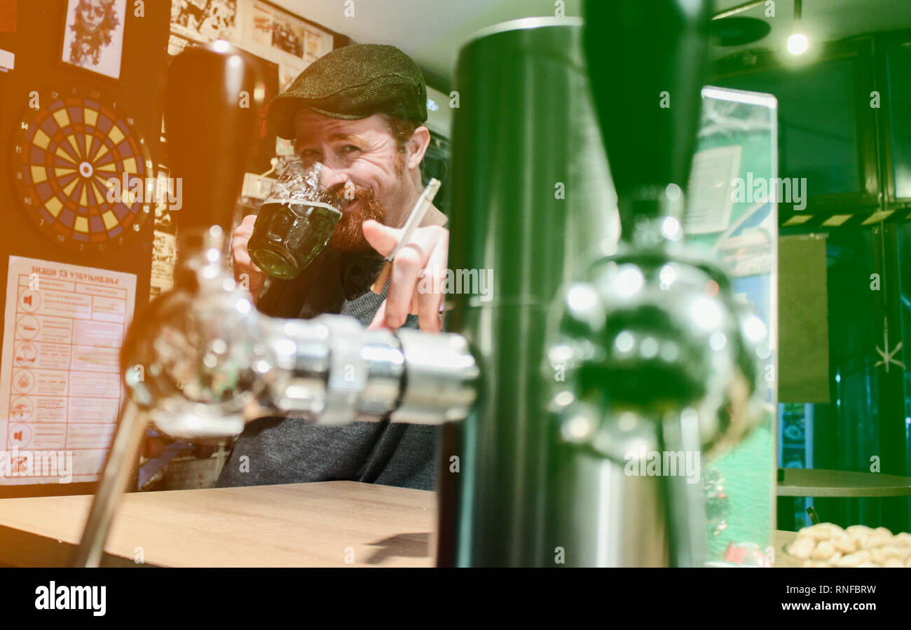 Good guy Irish smokes cigarette and drink beer and calling zou to join in pub during St Patrick Day (filter represent Irish flag) Stock Photo