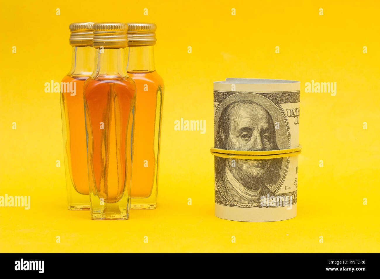 Small bottles with alcohol on a yellow background and money dollars