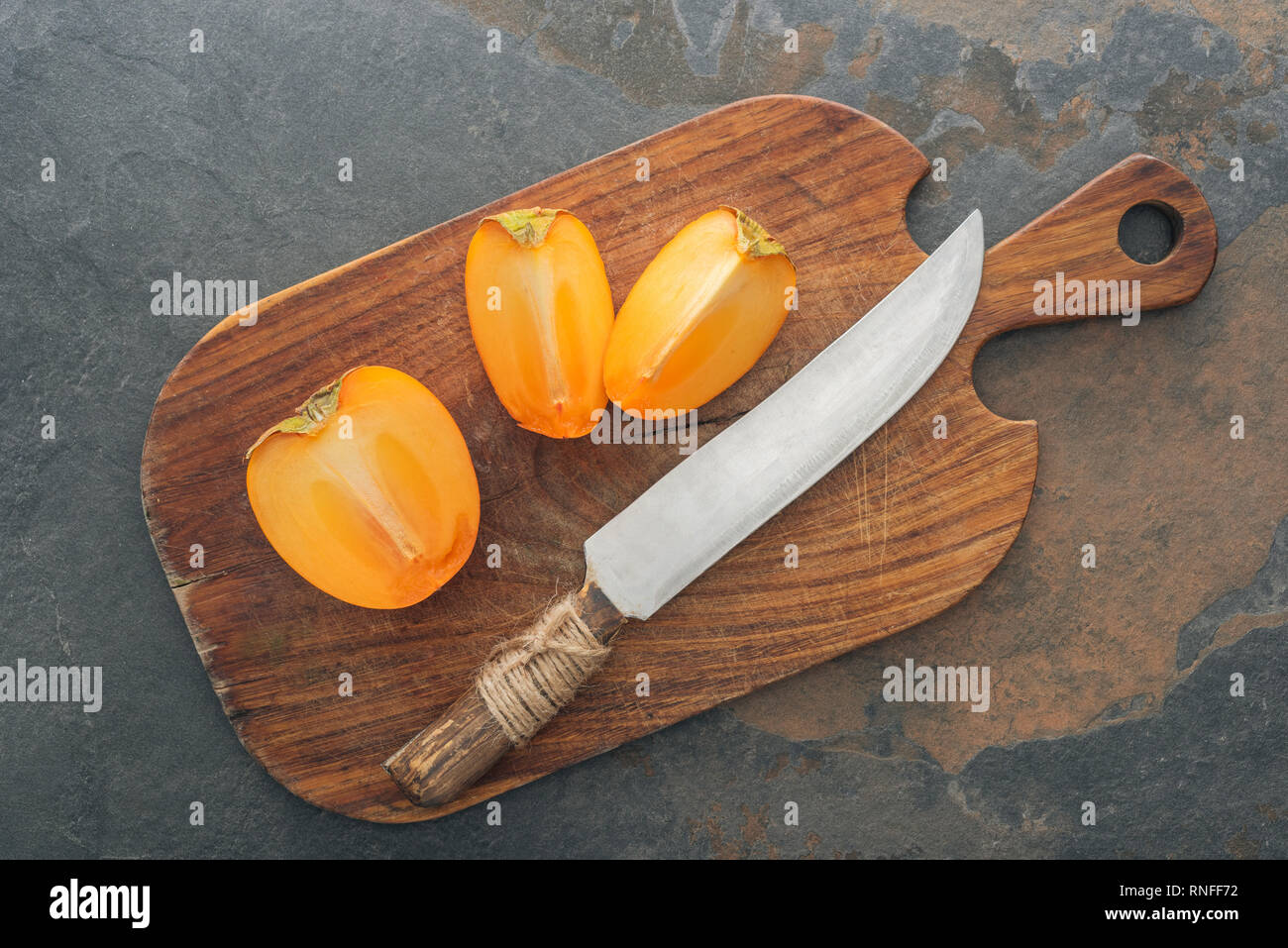cut ripe tasty persimmons on cutting board with knife Stock Photo