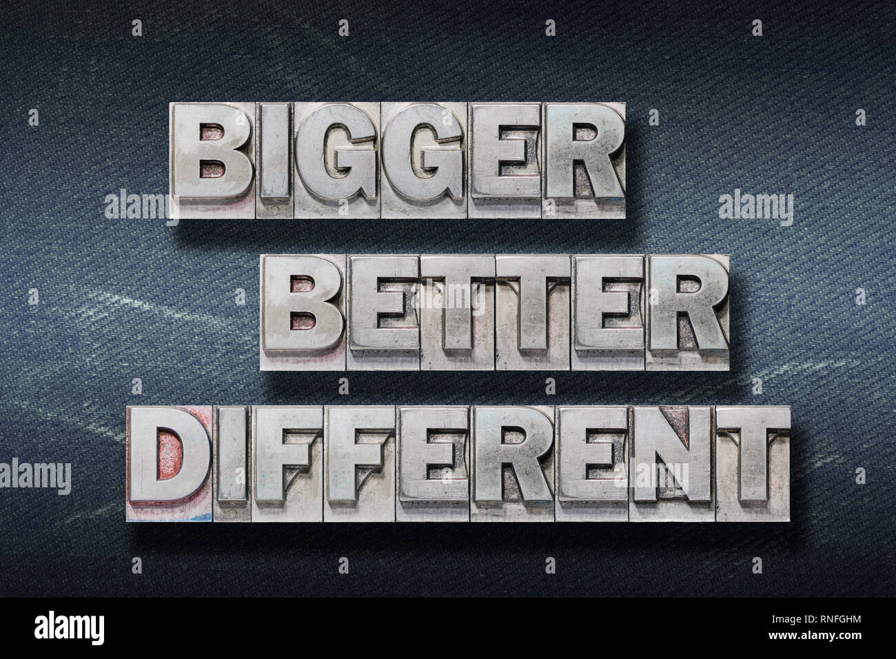 bigger, better, different words made from metallic letterpress on dark jeans background Stock Photo
