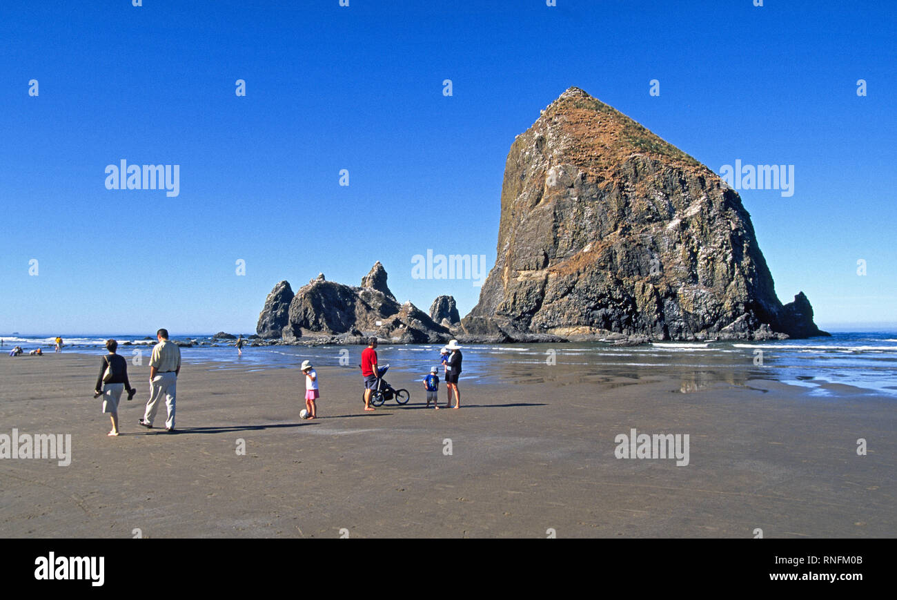 Visitors walk the beach near Haystack Rock, a towering seastack near ...