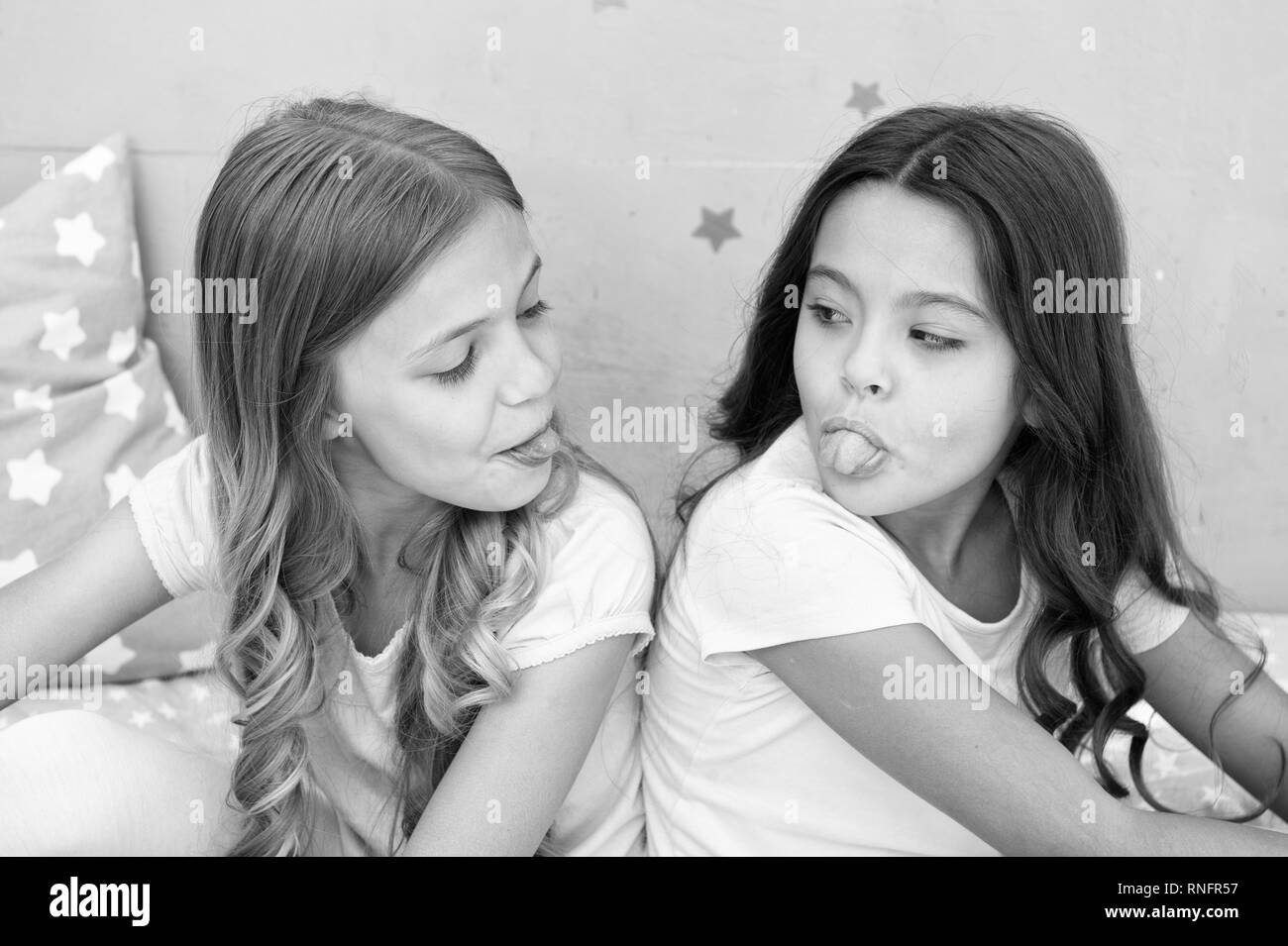 Children show tongue each other. Relations sisters or best friends. Overcome relations issues. Childhood friendship. Friends sit back to back show tongues. Grimace and emotion. Antics showing tongue. Stock Photo