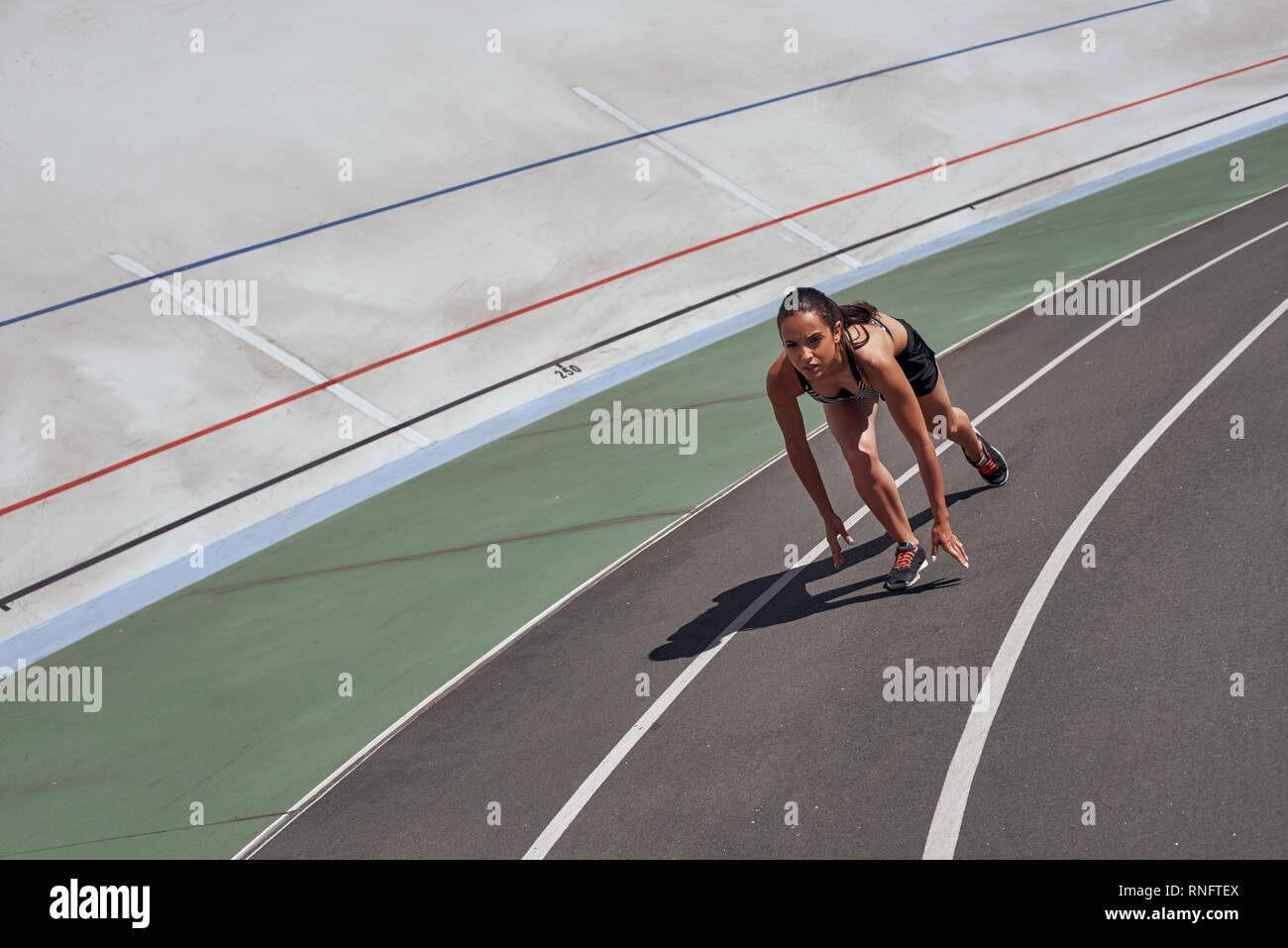 Young woman wearing black sportswear is ready to run on racetrack ...