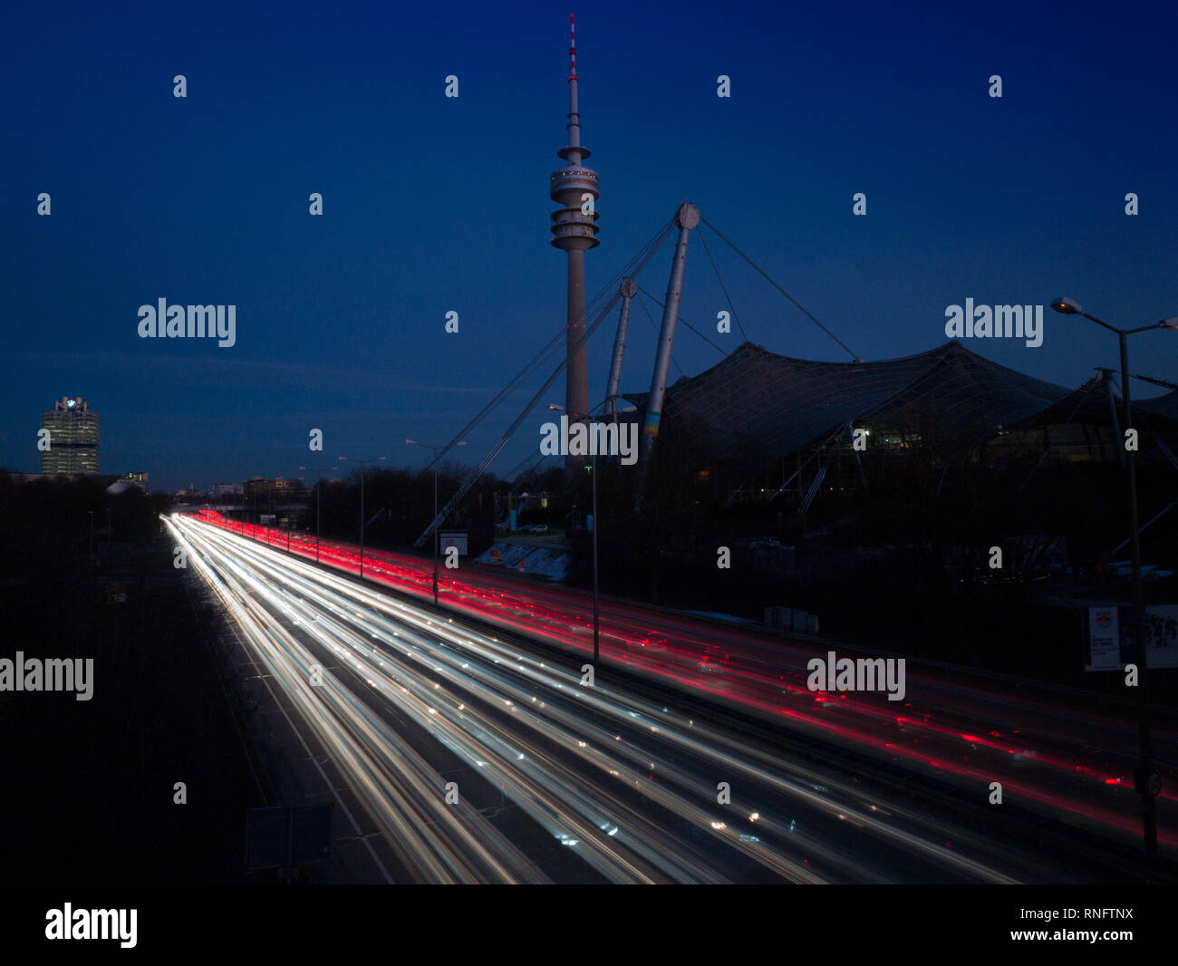 Munich, Germany - February 14th 2019: Olympia tower and olympia stadium Munich with diagonal rush hour traffic lights in bulb exposure during dawn Stock Photo