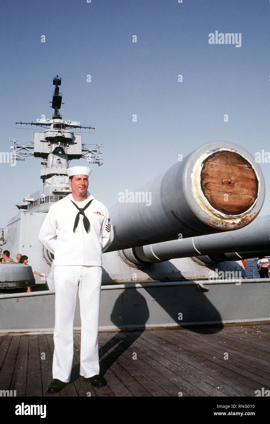 A crewman in a dress white uniform stands near Mark 7 16-inch/50-caliber guns on the forward deck of the battleship USS NEW JERSEY (BB-62).  The ship was recently towed here for refitting and reactivation. Stock Photo