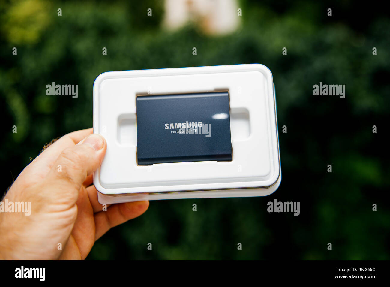 PARIS, FRANCE - AUG 14, 2018: Man hand holding plastic box of Samsung T5 Portable SSD 2 tb external hard drive disk with high read and write speed against green background unboxing testing  Stock Photo
