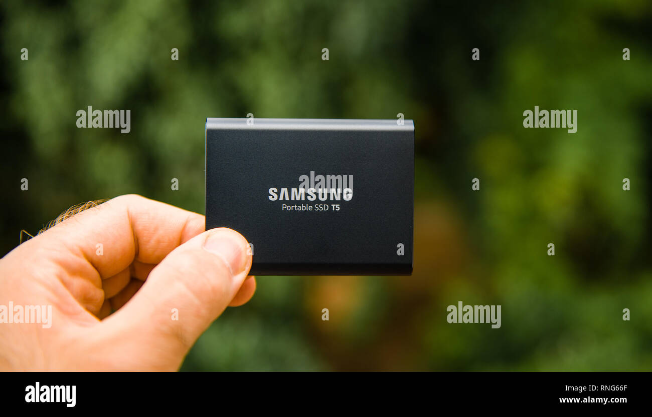 PARIS, FRANCE - AUG 14, 2018: Man hand presenting holding Samsung T5 Portable SSD 2 tb external hard drive disk with high read and write speed against green background unboxing testing  Stock Photo