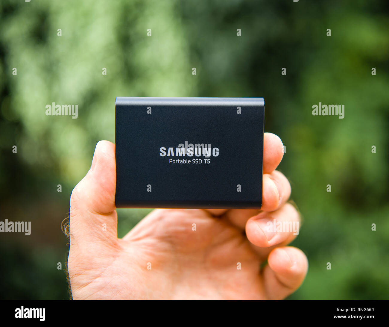 PARIS, FRANCE - AUG 14, 2018: Man hand holding Samsung T5 Portable SSD 2 tb external hard drive disk with high read and write speed against green background unboxing testing  Stock Photo