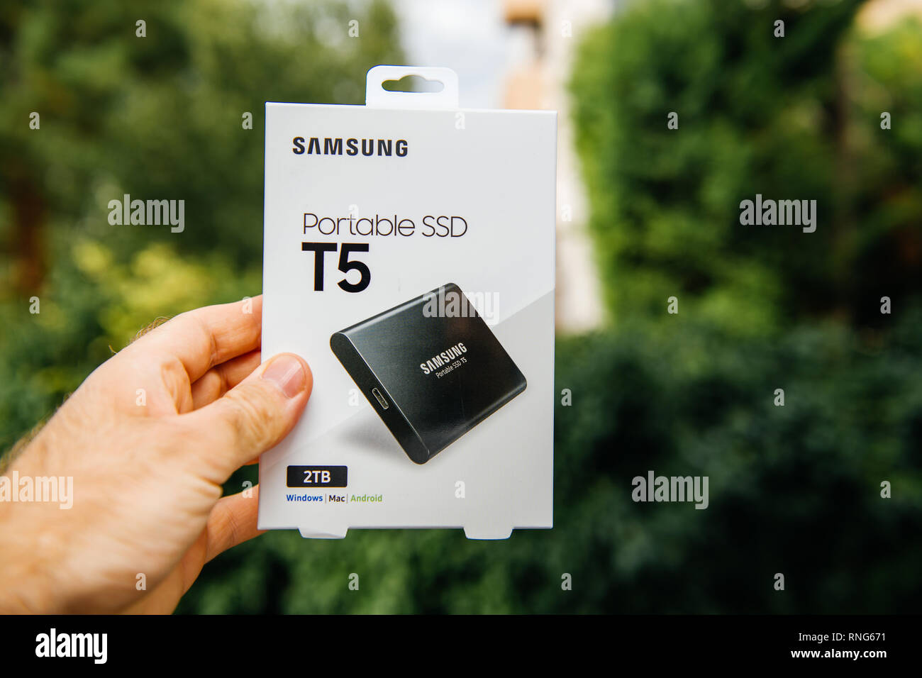 PARIS, FRANCE - AUG 14, 2018: Man hand holding new box of Samsung T5 Portable SSD external hard drive disk with high read and write speed against green background unboxing testing  Stock Photo