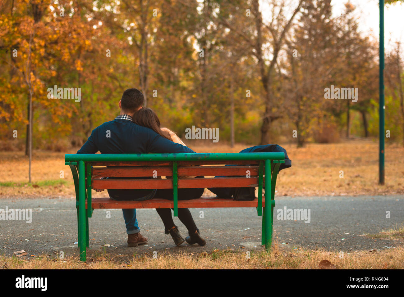 Young sweet couple embrace on a bench in park watching a beautiful ...