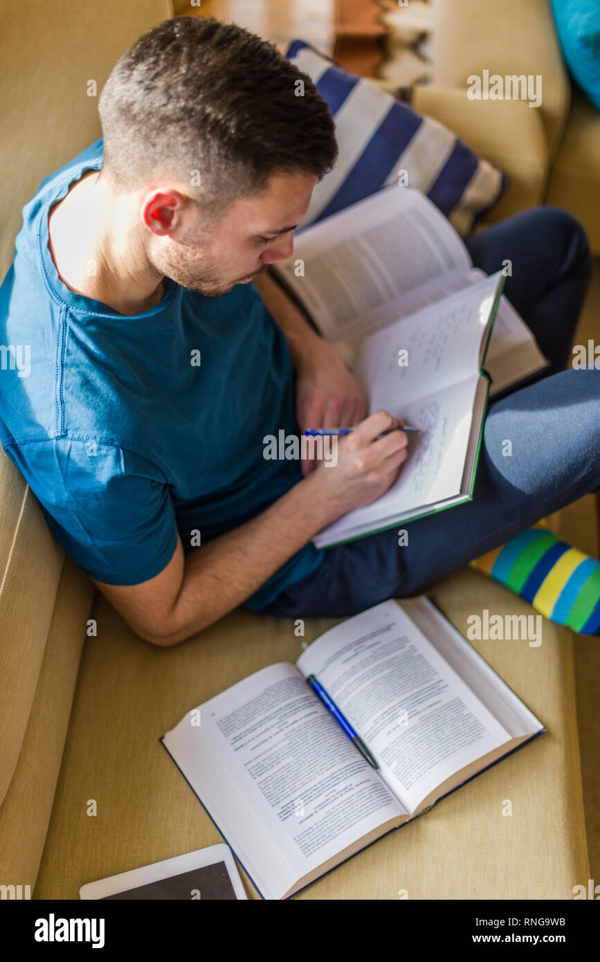 A handsome man is taking notes while learning from the book Stock Photo