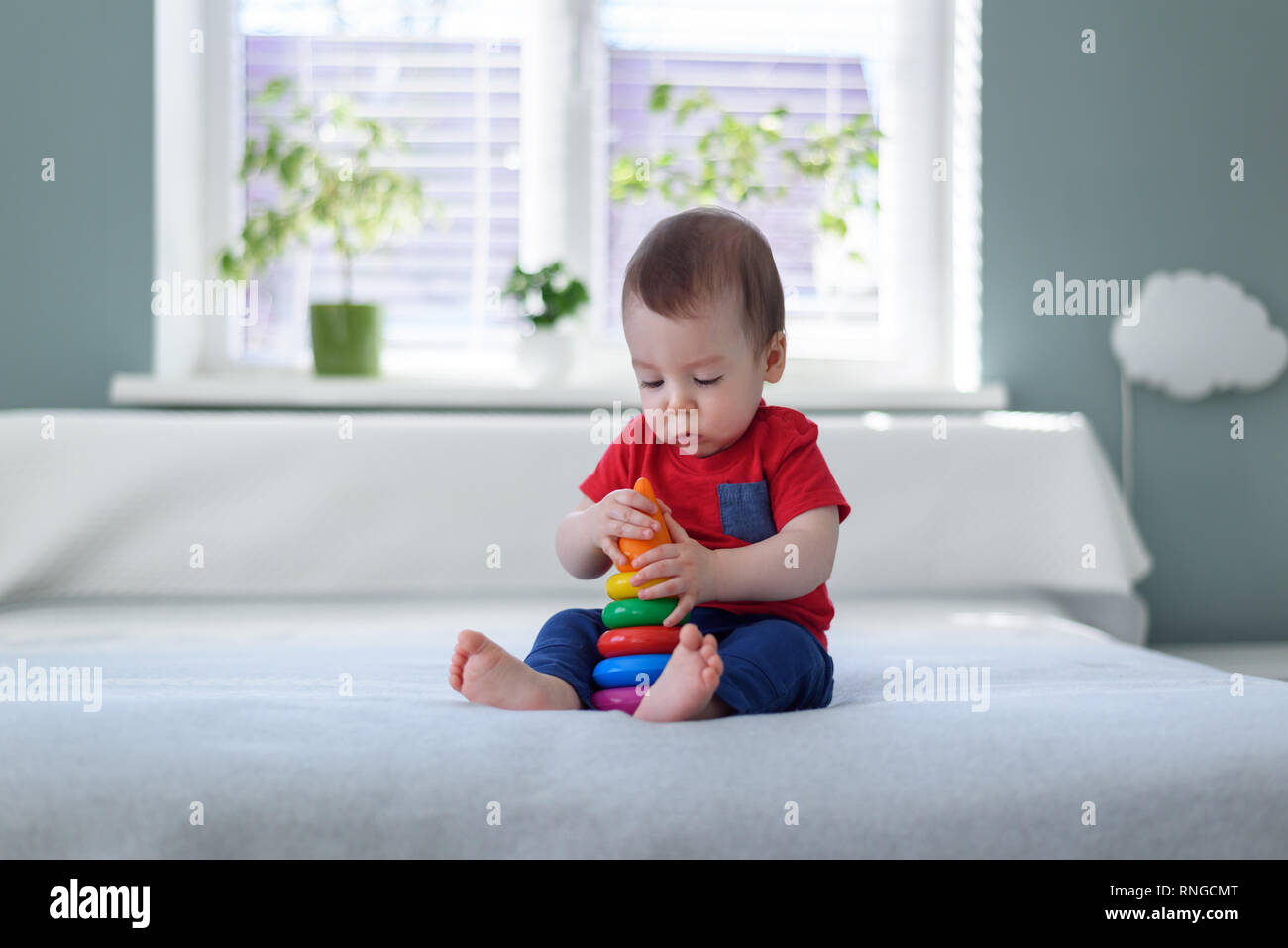 Baby boy with coloured pyramid toy on bed in his room Stock Photo