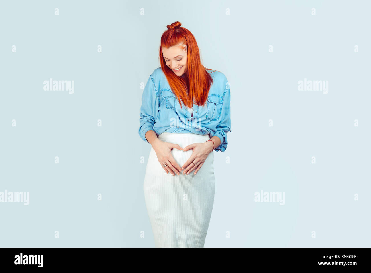 Wonderful young woman with ginger hair holding hands in heart of shape looking down at her