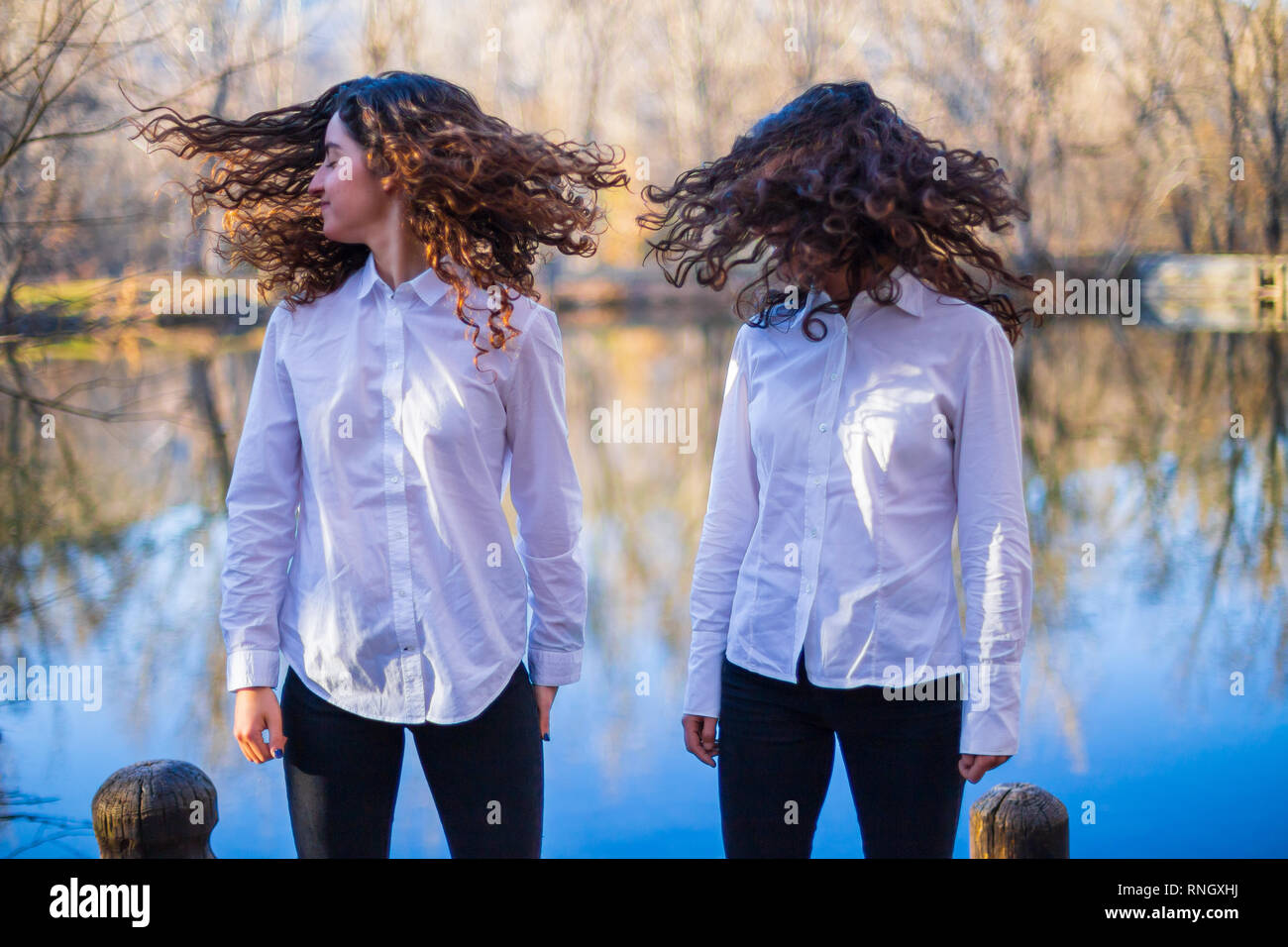 Young twin sisters in same clothes shaking hair at lake on autumn day in the forest Stock Photo