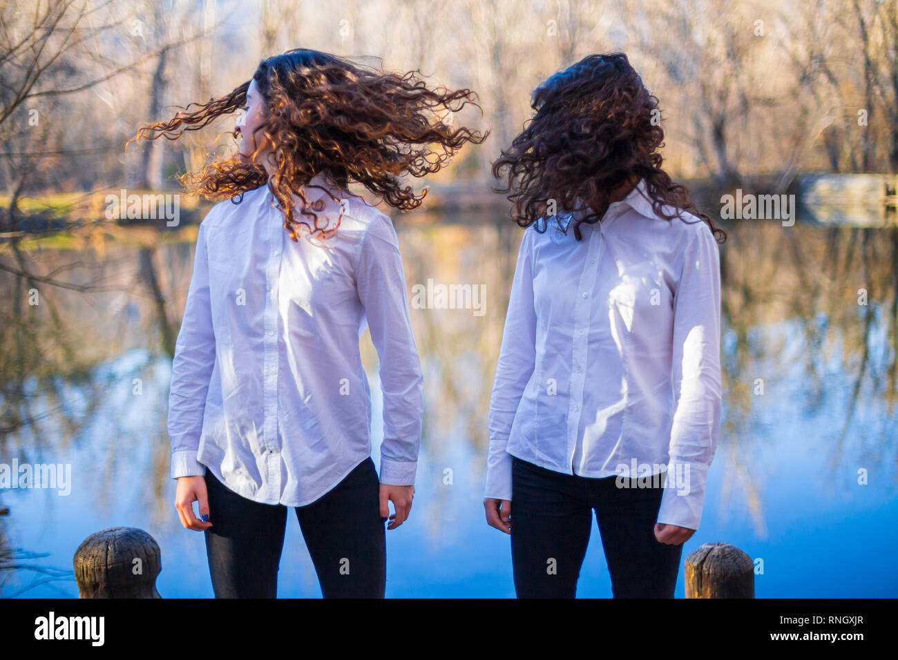 Young twin sisters in same clothes shaking hair at lake on autumn day ...