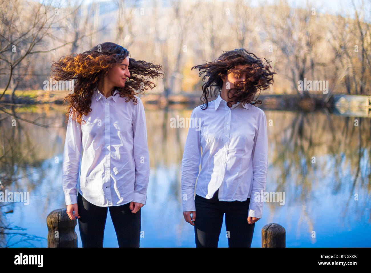 Young twin sisters in same clothes shaking hair at lake on autumn day in the forest Stock Photo
