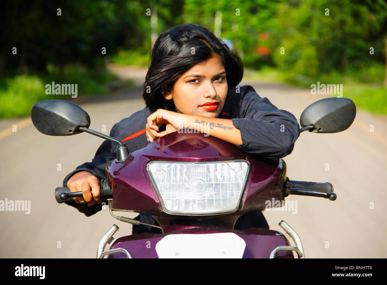 Close-up of young Indian girl resting on two wheeler scooter handle and posing for camera, Pune Stock Photo