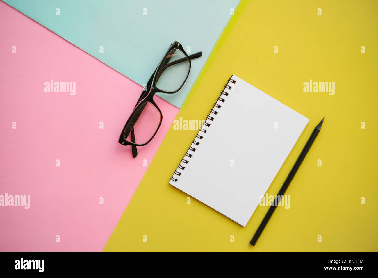 Notepad, glasses and a pencil on a multi-colored background. Stock Photo