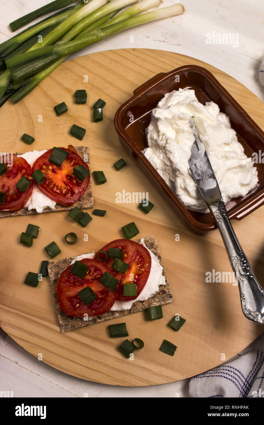 healthy and vegetarian breakfast with crispbread, quark, tomatoes and spring onions on a wooden board Stock Photo