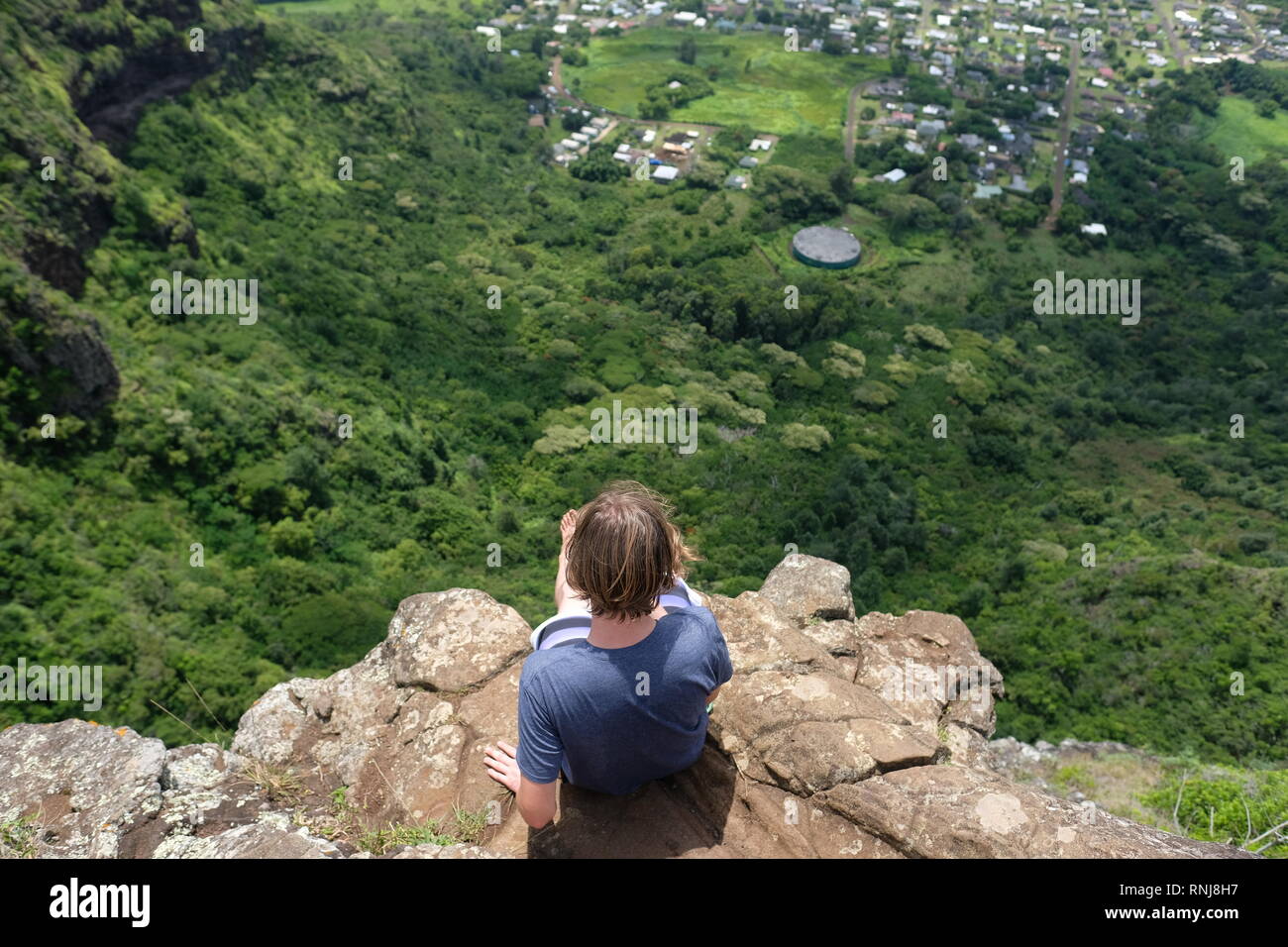 Boy on a cliffs edge overlooking a valley. The view is from the top of Sleeping Giant hiking trail on the island of Kaua'i, Hawaii. Stock Photo