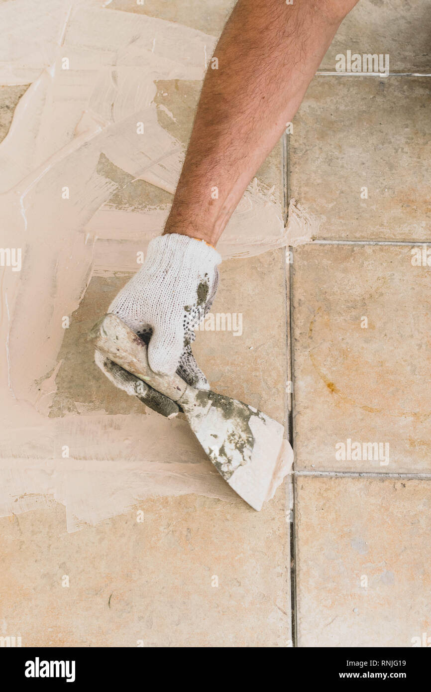 Man hand with trowel plastering a tiles, with spacle, laying tiles