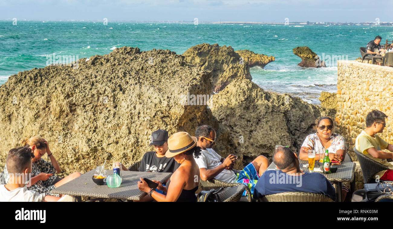 People tourists looking at their mobile phone cellphones at The Rock Bar at Ayana Resort and Spa Jimbaran Bali Indonesia. Stock Photo