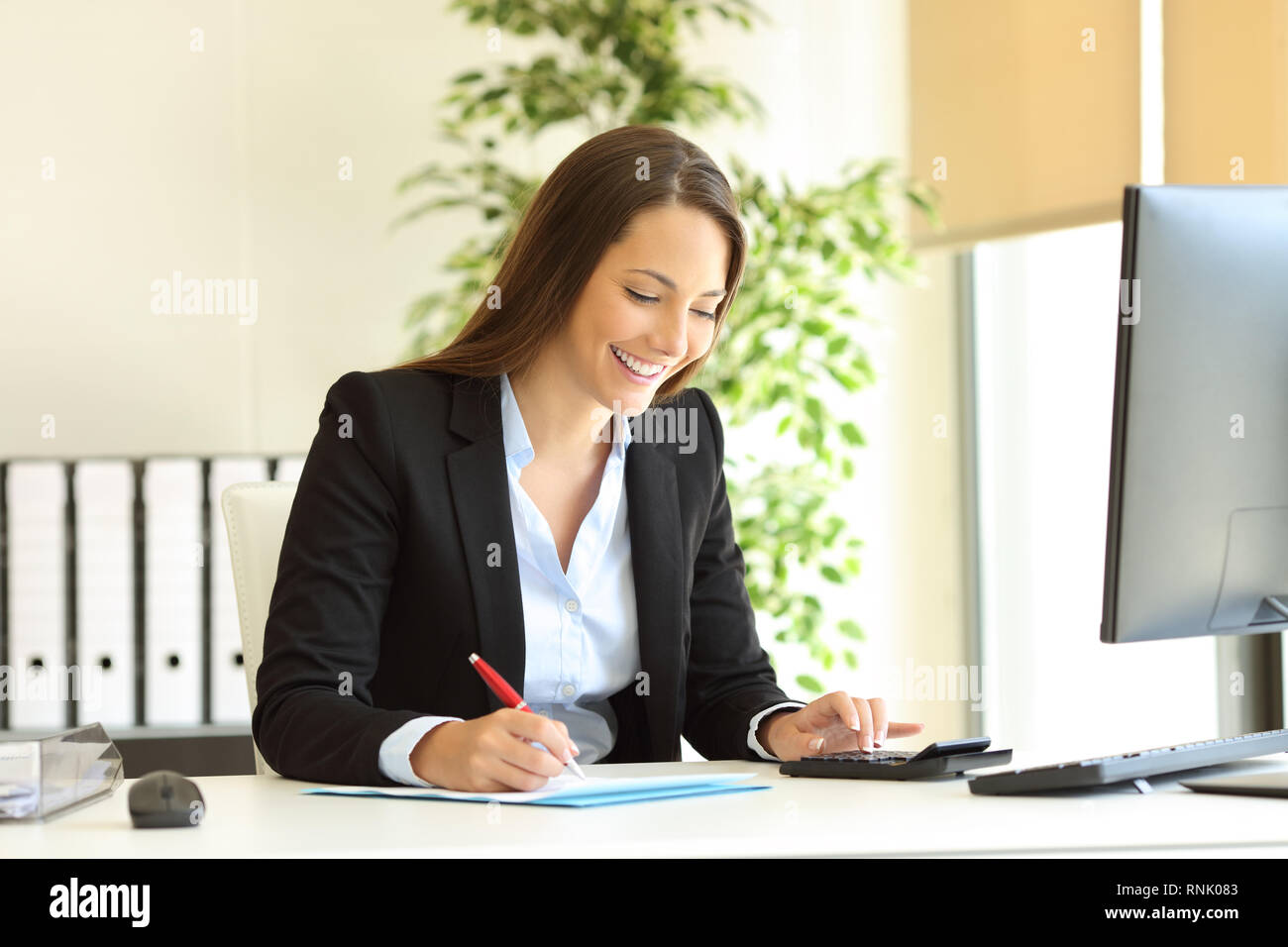 Happy office worker working calculating and writing budget on a desktop Stock Photo